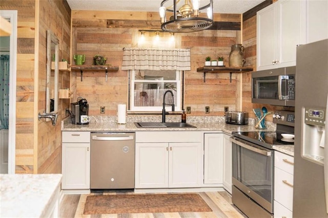 kitchen with sink, wooden walls, stainless steel appliances, light stone countertops, and white cabinets