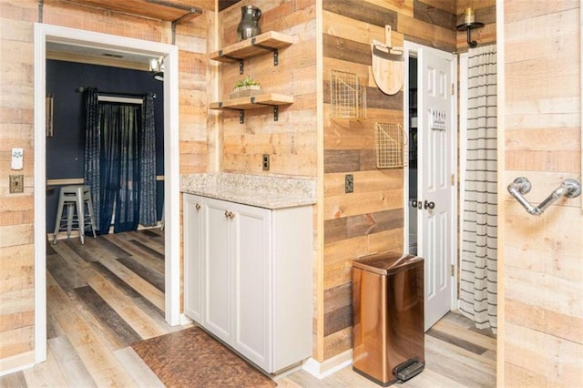 interior space with white cabinetry, wooden walls, light hardwood / wood-style floors, and light stone counters