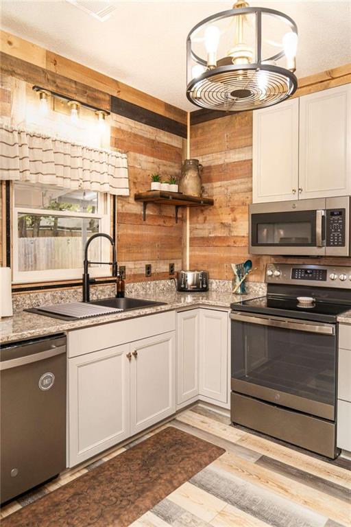 kitchen with appliances with stainless steel finishes, wooden walls, light hardwood / wood-style floors, and white cabinets