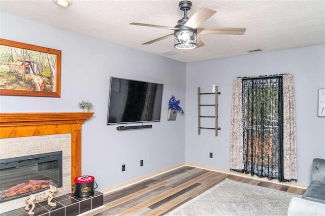 living room with hardwood / wood-style floors, a tile fireplace, a textured ceiling, and ceiling fan