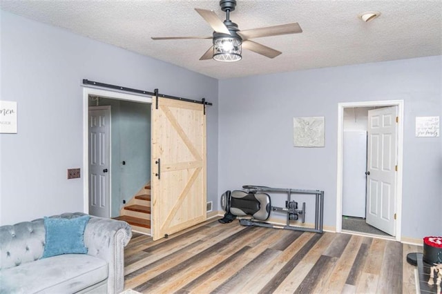 living room with ceiling fan, wood-type flooring, a barn door, and a textured ceiling