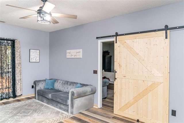 sitting room featuring wood-type flooring, a barn door, ceiling fan, and a textured ceiling