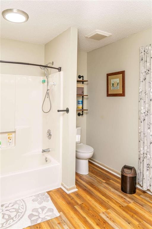 bathroom featuring hardwood / wood-style floors, shower / bathtub combination with curtain, a textured ceiling, and toilet