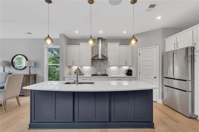 kitchen with a kitchen island with sink, wall chimney range hood, stainless steel fridge, and decorative light fixtures