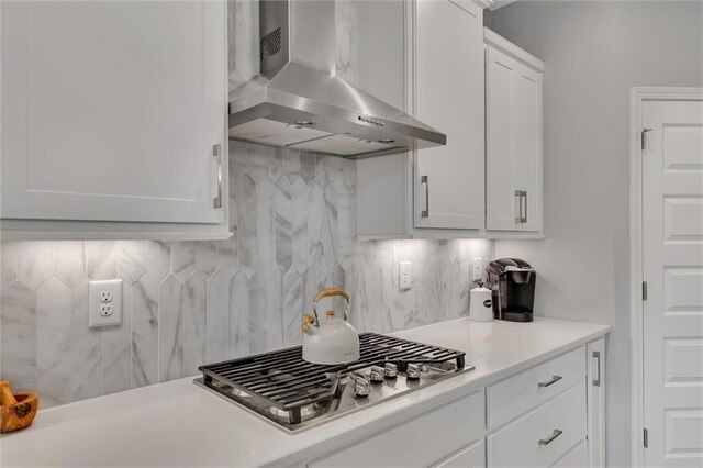 kitchen with backsplash, wall chimney exhaust hood, stainless steel gas cooktop, and white cabinets