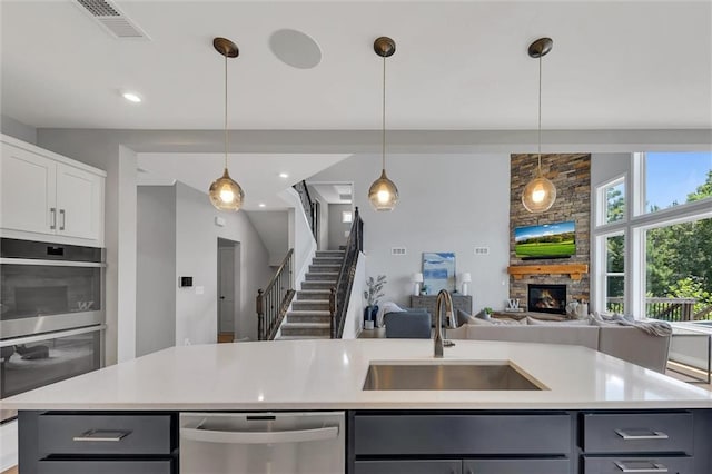 kitchen with stainless steel dishwasher, sink, decorative light fixtures, and a kitchen island with sink