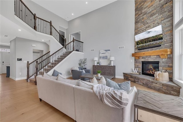 living room featuring a stone fireplace, light wood-type flooring, and a high ceiling