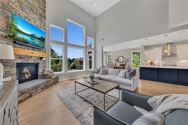 living room featuring a towering ceiling, a stone fireplace, a healthy amount of sunlight, and light hardwood / wood-style flooring