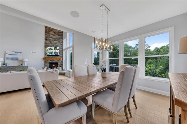 dining room featuring a stone fireplace, an inviting chandelier, and light wood-type flooring