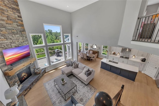 living room featuring a stone fireplace, a towering ceiling, sink, and light hardwood / wood-style floors