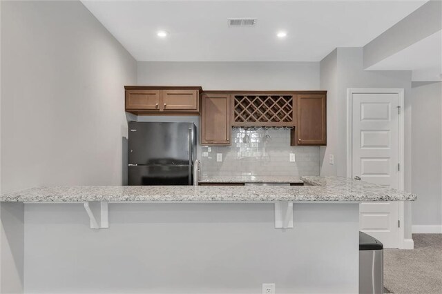 kitchen with a breakfast bar area, tasteful backsplash, light stone counters, light carpet, and black refrigerator