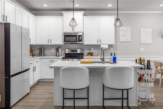 kitchen with pendant lighting, white cabinetry, a kitchen island with sink, stainless steel appliances, and light wood-type flooring