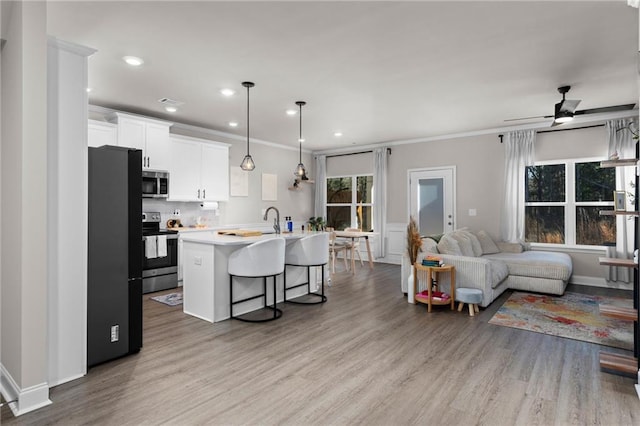 kitchen featuring a breakfast bar, appliances with stainless steel finishes, white cabinets, a center island with sink, and decorative light fixtures