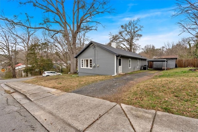 view of side of home with a yard, driveway, fence, and a chimney