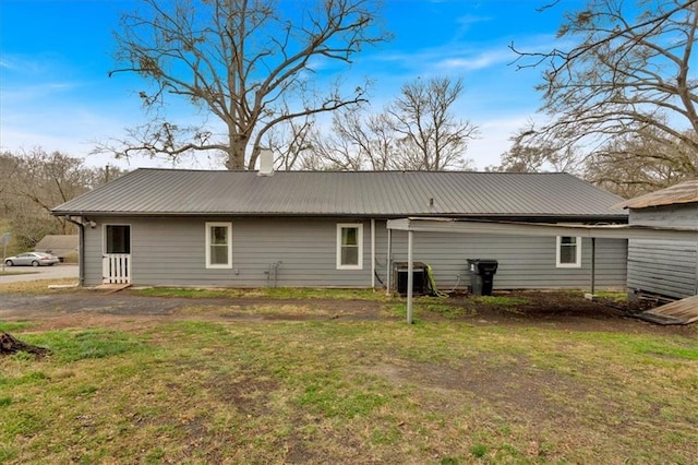 rear view of house featuring metal roof, central AC, a chimney, and a lawn