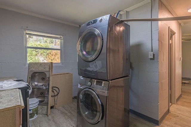 clothes washing area featuring light hardwood / wood-style flooring, stacked washer and clothes dryer, and crown molding