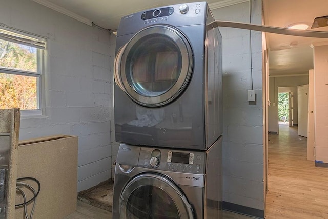 laundry area with stacked washing maching and dryer, crown molding, and light hardwood / wood-style flooring