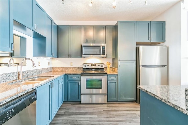 kitchen featuring light stone counters, a textured ceiling, light hardwood / wood-style flooring, sink, and stainless steel appliances