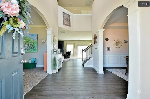 foyer with a towering ceiling, ornate columns, and dark hardwood / wood-style floors