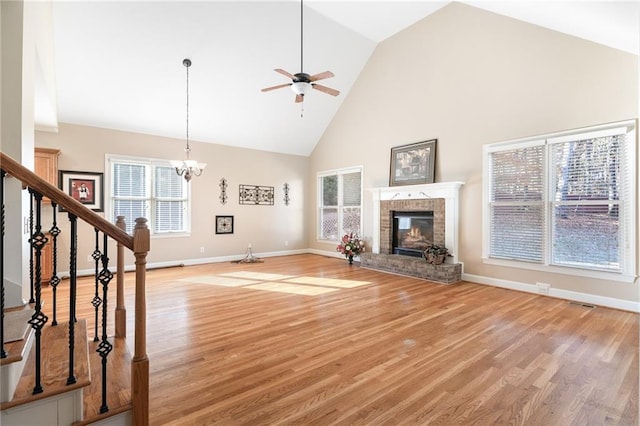 unfurnished living room with plenty of natural light, light wood-type flooring, ceiling fan with notable chandelier, and high vaulted ceiling