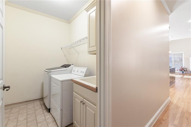 laundry room with cabinets, light wood-type flooring, crown molding, and washing machine and clothes dryer