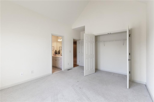 unfurnished bedroom with high vaulted ceiling, light colored carpet, connected bathroom, and a closet