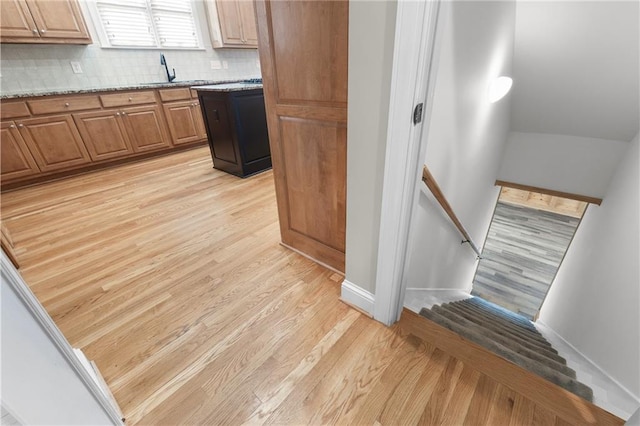 kitchen with decorative backsplash, light hardwood / wood-style flooring, light stone countertops, and sink