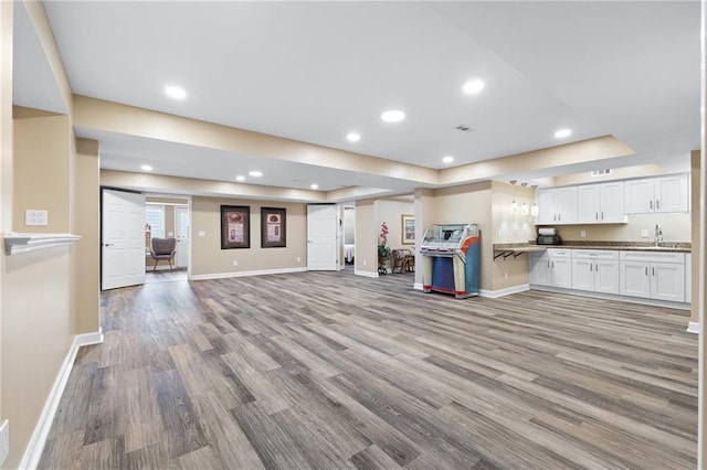 unfurnished living room with a tray ceiling, light hardwood / wood-style flooring, and sink