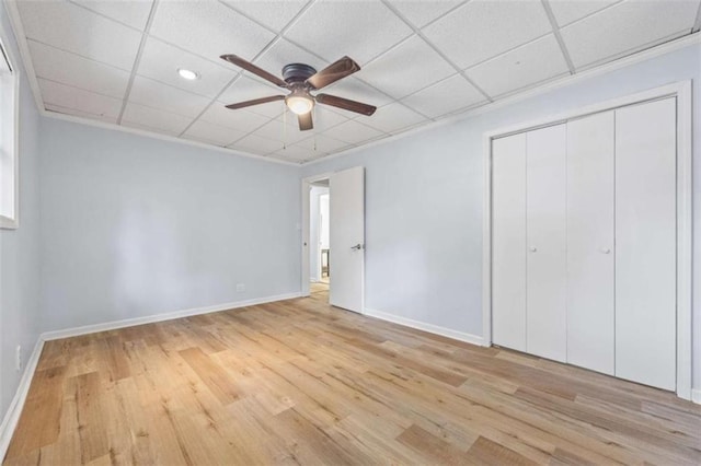 unfurnished bedroom with light wood-type flooring, a paneled ceiling, and a closet