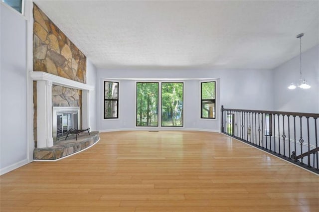 unfurnished living room with light wood-type flooring, a chandelier, plenty of natural light, and a fireplace