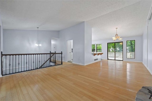 unfurnished room with light wood-type flooring, vaulted ceiling, a textured ceiling, and an inviting chandelier