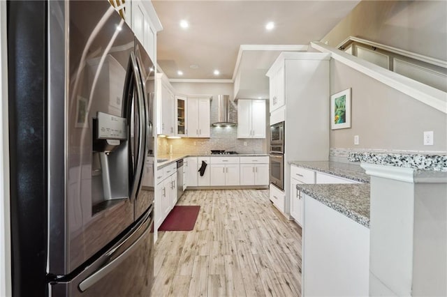 kitchen featuring appliances with stainless steel finishes, tasteful backsplash, light stone countertops, wall chimney exhaust hood, and white cabinets