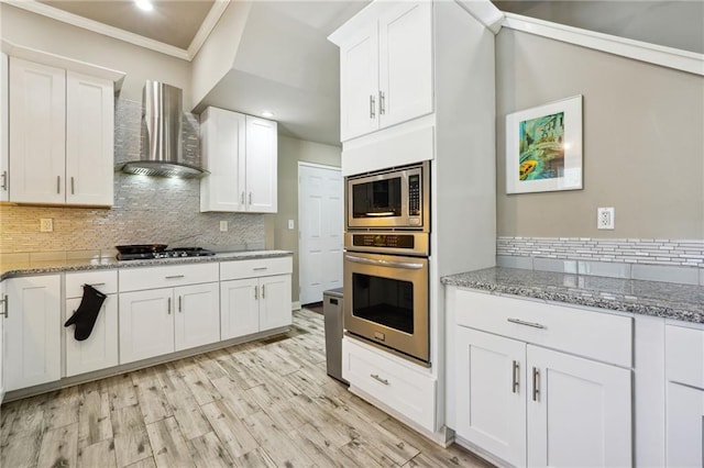 kitchen featuring stainless steel appliances, wall chimney exhaust hood, and white cabinetry