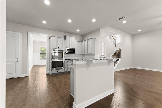 427 Dawson Pointe Pkwy, Dawsonville, GA 30534 - kitchen with appliances with stainless steel finishes, a breakfast bar, a peninsula, dark wood-type flooring, and light stone countertops