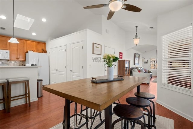 dining area with ceiling fan, lofted ceiling with skylight, and dark wood-type flooring