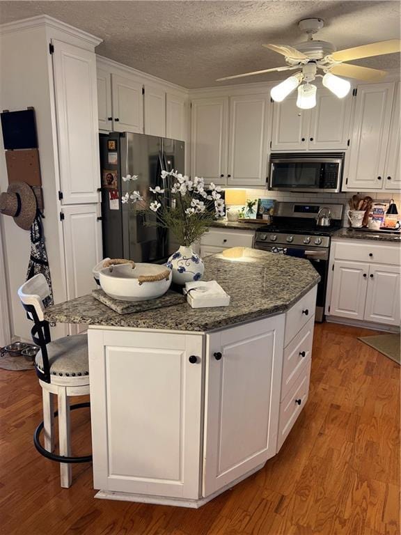 227 Bennett Farms Trl, Acworth, GA 30102 - kitchen featuring appliances with stainless steel finishes, white cabinetry, a center island, wood finished floors, and a textured ceiling