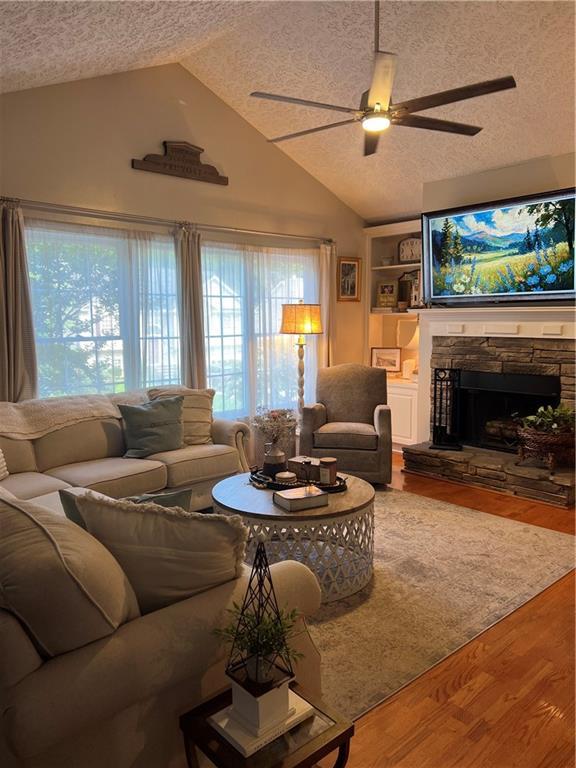 227 Bennett Farms Trl, Acworth, GA 30102 - living room featuring a textured ceiling, vaulted ceiling, ceiling fan, wood finished floors, and a fireplace