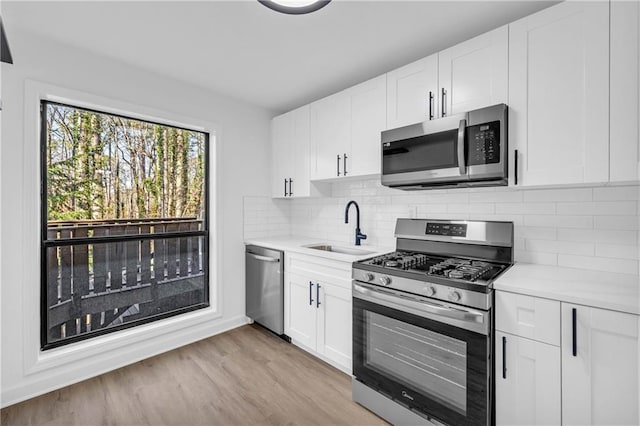 kitchen with sink, light wood-type flooring, stainless steel appliances, decorative backsplash, and white cabinets