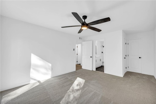 unfurnished bedroom with ensuite bathroom, ceiling fan, and dark colored carpet