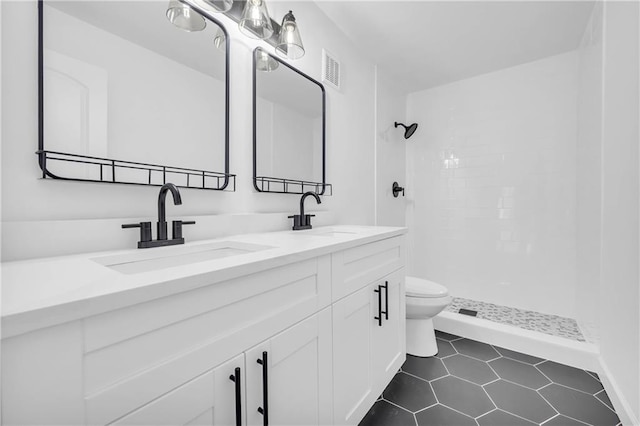 bathroom featuring vanity, a tile shower, tile patterned floors, and toilet