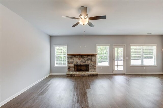 unfurnished living room featuring dark hardwood / wood-style flooring, a stone fireplace, plenty of natural light, and ceiling fan