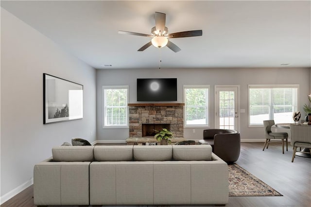 living room with wood-type flooring, a stone fireplace, and ceiling fan