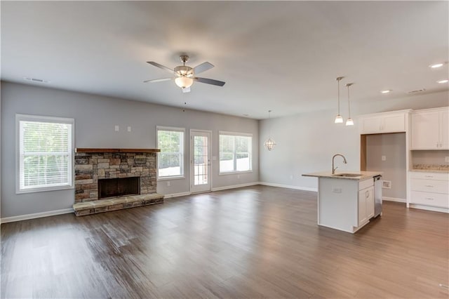 kitchen featuring ceiling fan, white cabinets, a stone fireplace, hanging light fixtures, and an island with sink