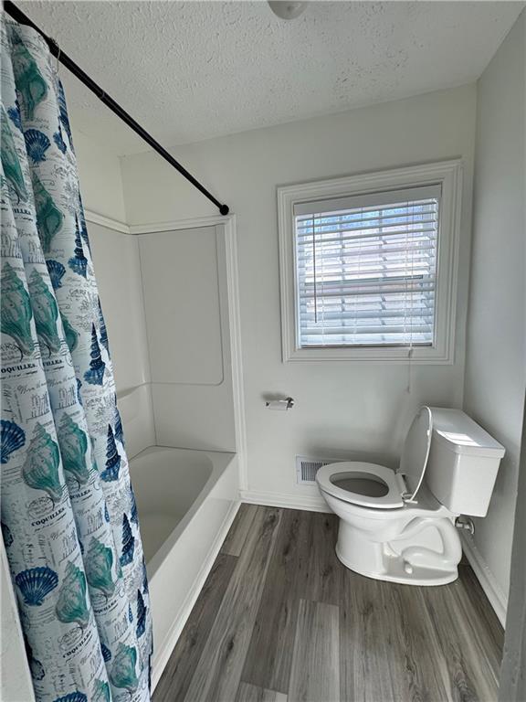 bathroom featuring toilet, wood-type flooring, shower / bath combination with curtain, and a textured ceiling