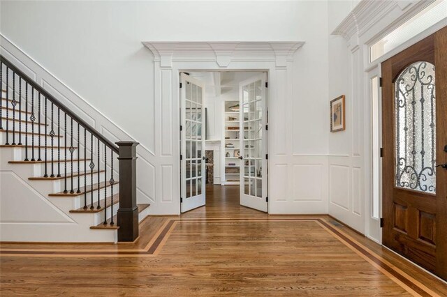 foyer entrance featuring french doors, wood finished floors, stairway, a wainscoted wall, and a decorative wall