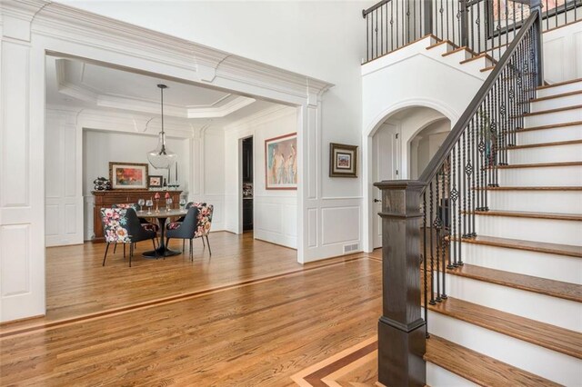 entrance foyer featuring a decorative wall, wood finished floors, stairway, ornamental molding, and a tray ceiling