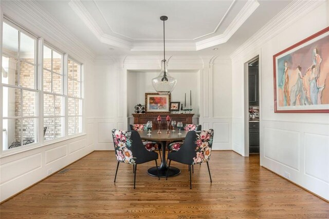 dining room with plenty of natural light, a decorative wall, a tray ceiling, and wood finished floors