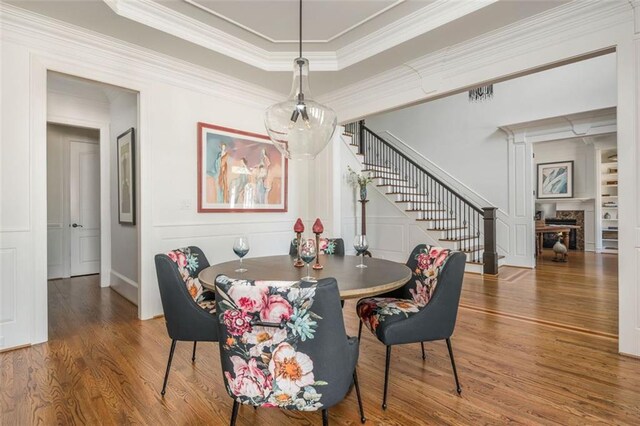 dining space featuring crown molding, stairs, a decorative wall, wood finished floors, and a fireplace