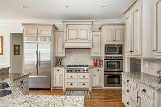 kitchen featuring light wood-type flooring, built in appliances, cream cabinets, and tasteful backsplash