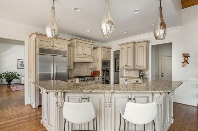 kitchen with cream cabinets, built in appliances, light stone counters, and tasteful backsplash